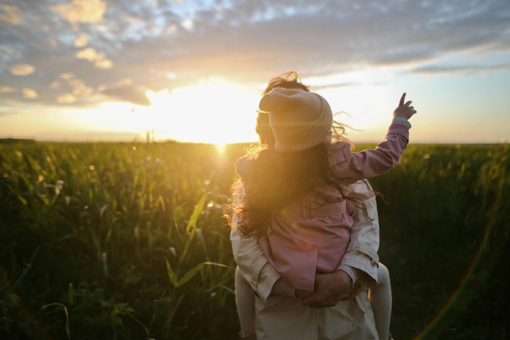 Frau Mit kind auf arm im Sonnenuntergrang, dank Wickelrucksack entspannt