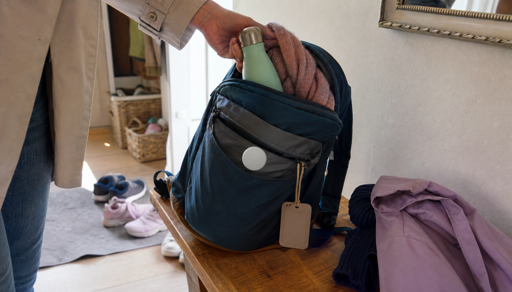 Kinderrucksack mit generischem Tracker, Namensschild ohne Text und Elternhand beim Packen