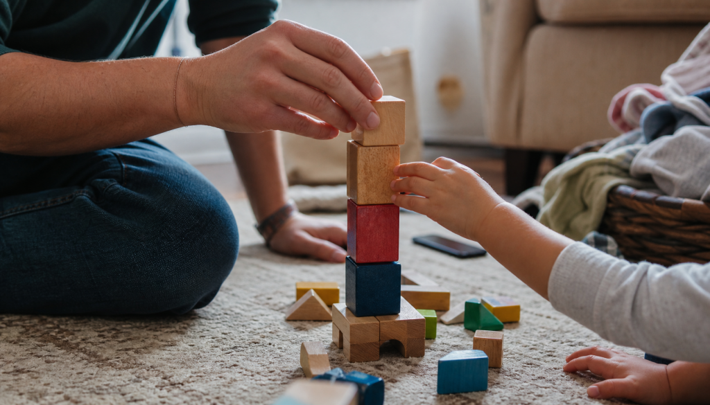 Eltern- und Kinderhände bauen langsam mit Holzklötzen auf dem Wohnzimmerboden