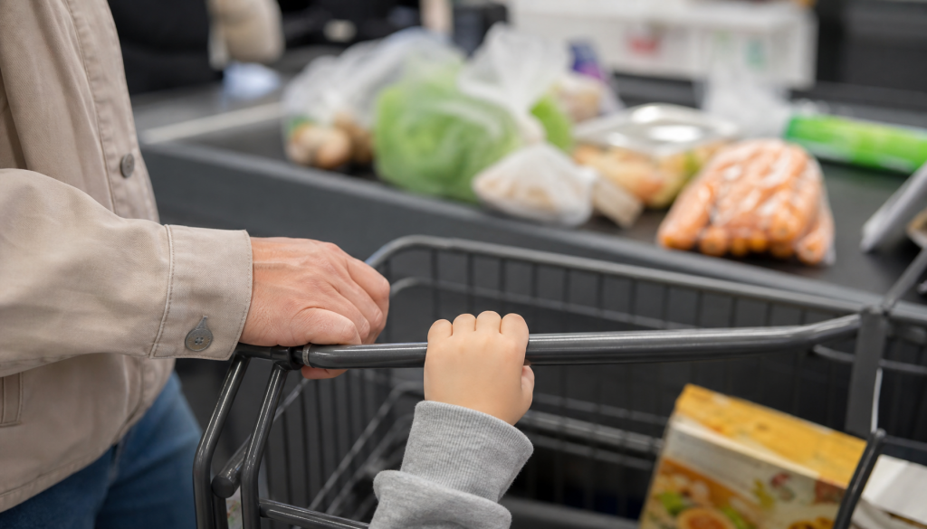 Ruhige Einkaufssituation mit Kinderhand am Einkaufswagen und kleiner Snackbox an der Kasse
