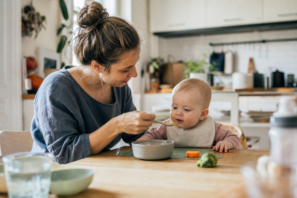 Baby sitzt am Familientisch und schaut neugierig auf ersten Brei und weiches Fingerfood